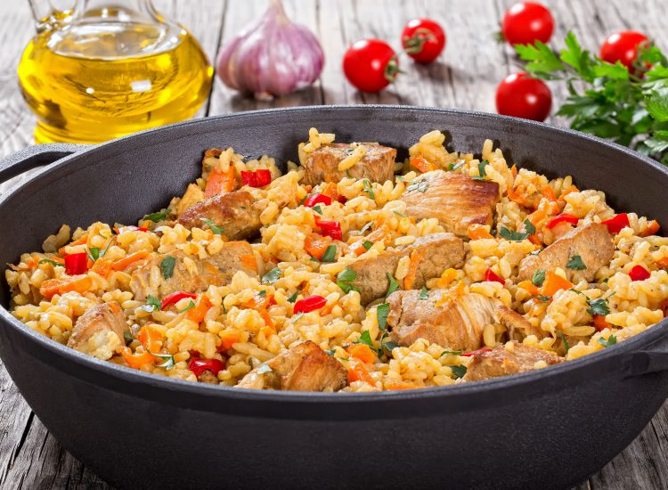 64036365 - homemade prepared paella with meat, pepper, vegetables and spices in iron stewpan on wooden planks,  bottle of olive oil,tomatoes,  parsley, garlic on background, close-up,  view from above